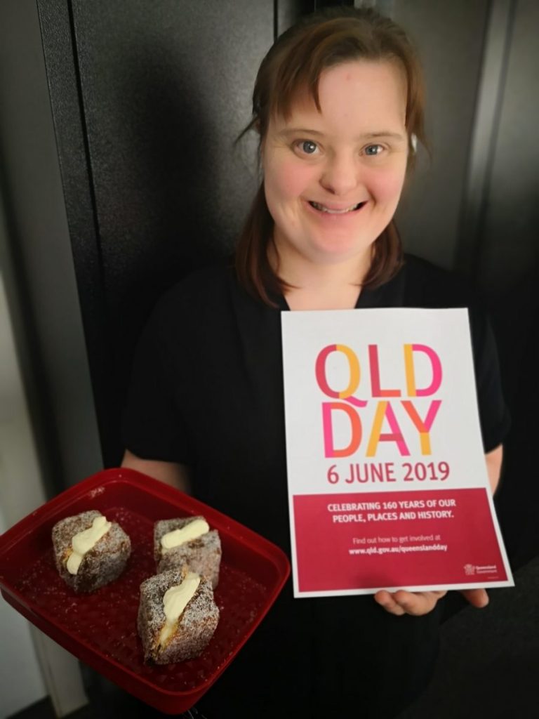 Sophie holding a plate of lamingtons and a flyer promoting Queensland Day.