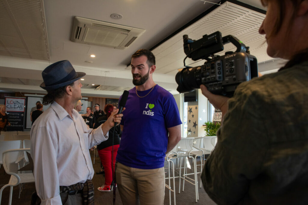 Man with a disability interviewing a person with an NDIS t-shirt